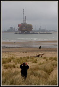 Man photographing woman on sea shore against sky