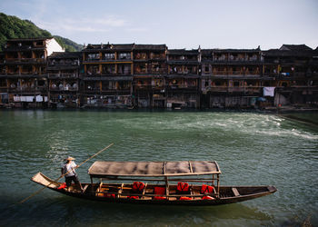 Man on gondola in canal against buildings during sunny day