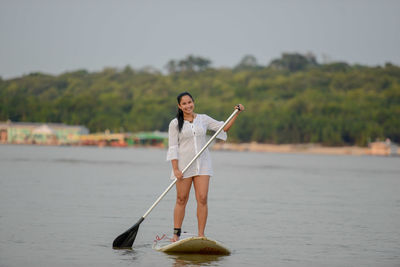 Portrait of young woman paddleboarding on sea during sunset