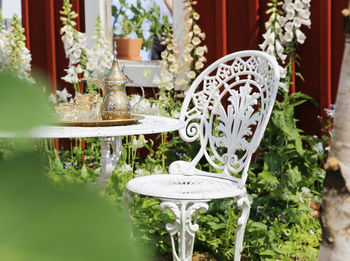 Cups with teapot on table by empty chair in yard