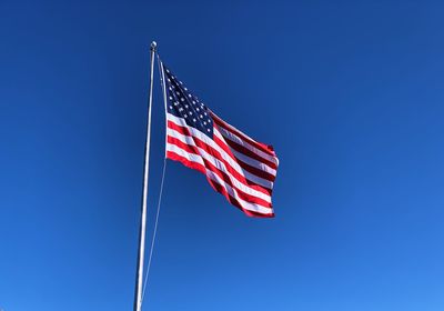 Low angle view of american flag waving against blue sky