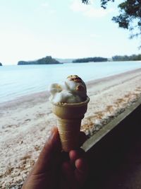 Cropped hand of person holding ice cream cone at beach