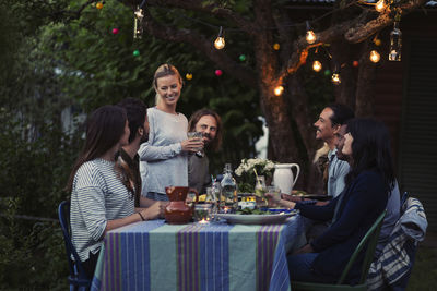 Happy woman talking to friends sitting at dinner table in yard