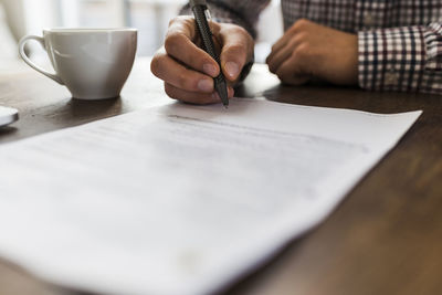 Close-up of man signing document on table