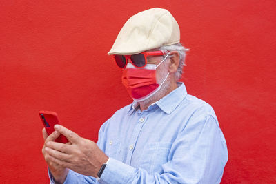 Senior man using smart phone standing against red background