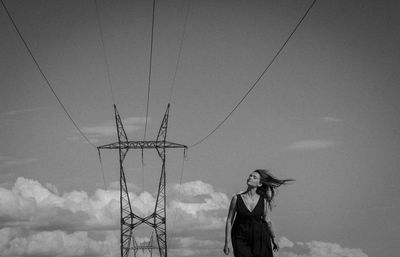 Low angle view of woman standing by electricity pylon against sky