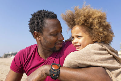 Happy girl with father sitting at beach on sunny day