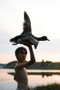 Side view of boy holding bird against sky