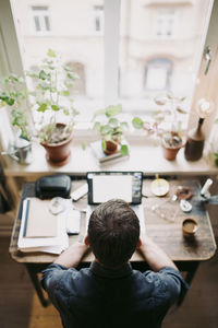 Rear view of man using laptop on table at home