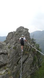 Rear view of hiker with backpack walking on rope against sky