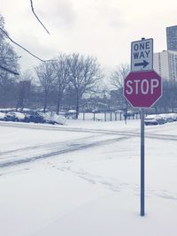 Road sign by snow covered trees against sky