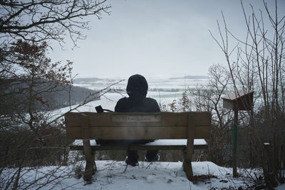 Rear view of man sitting on bench in winter