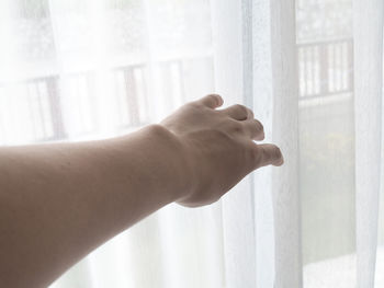 Cropped hand of woman touching curtain by window