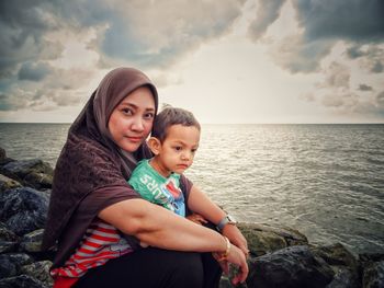Portrait of mother with daughter at beach against sky
