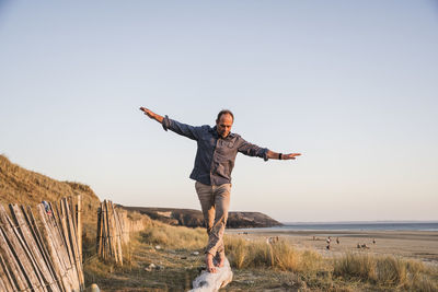 Mature man with arms outstretched walking on log