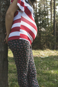 Midsection of pregnant woman standing against tree
