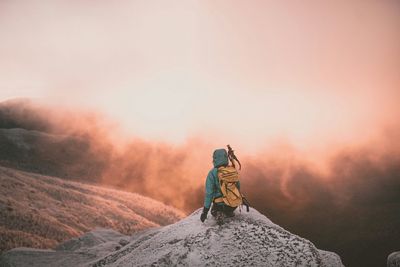 Rear view of hiker on mountain peak against cloudy sky during sunrise