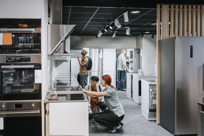 Saleswoman crouching while assisting customer in buying modern appliance at electronics store