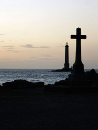Silhouette cross by sea against sky during sunset