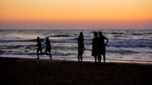 Silhouette people on beach against sky during sunset