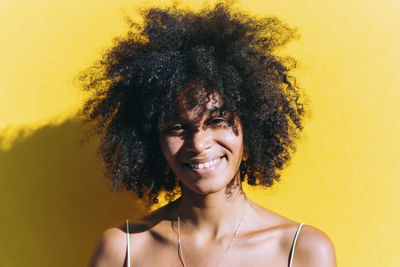 Happy woman with afro hairstyle in front of yellow wall