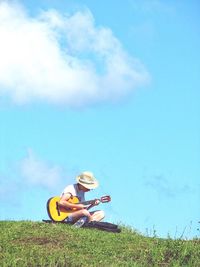 Man playing guitar on field against blue sky