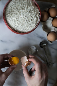 High angle view of hand holding egg over bowl