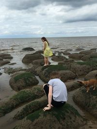 Boy and girl with dog on rocks against sea