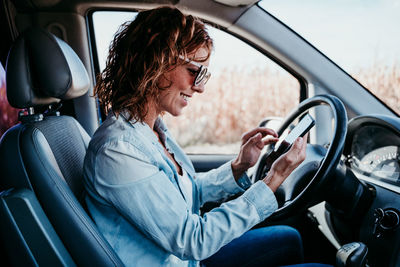 Side view of smiling woman using smart phone in camper trailer