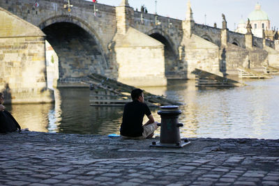 Rear view of man sitting on bridge over river