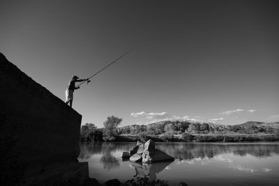 Man fishing in lake against sky