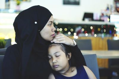 Close-up of mother with sleeping daughter sitting at restaurant
