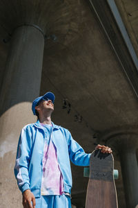 Low angle view of happy man with longboard standing under bridge at sunny day