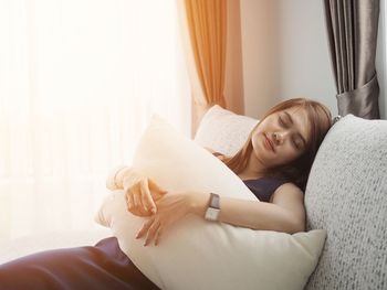 Woman embracing pillow while sitting on sofa at home