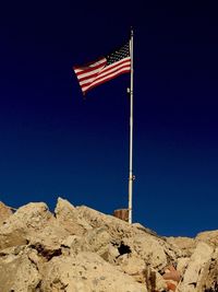 Low angle view of american flag on rocks against clear blue sky
