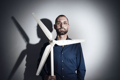 Businessman holding model of wind turbine in front of gray wall