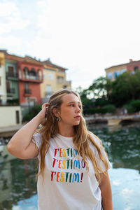 Tranquil young female with long hair standing on embankment in tropical city in summer evening