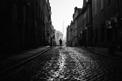 Man walking on street in city against sky