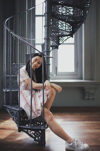 Portrait of smiling young woman sitting on spiral staircase at home