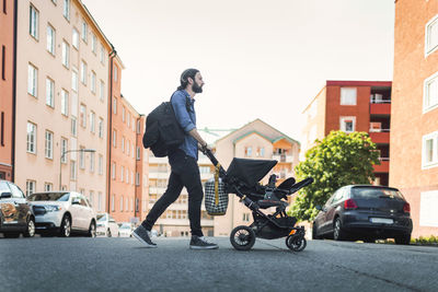 Full length side view of man pushing baby in carriage crossing city street