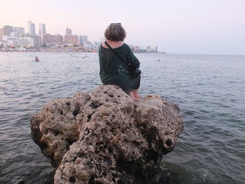 Man standing on rock by sea against sky