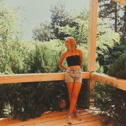 Rear view of woman standing by railing against trees