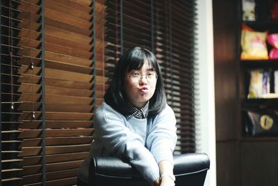 Portrait of young woman puckering on chair against window