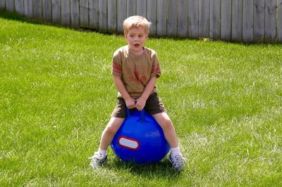 Boy sitting on blue fitness ball in back yard