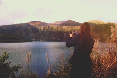 Rear view of woman photographing lake and mountains through phone