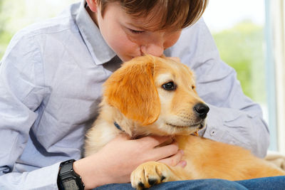 Cute boy kissing dog sitting window at home