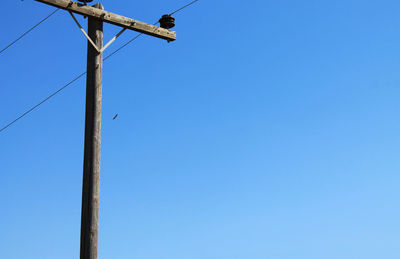 Low angle view of bird perching on cable against clear blue sky