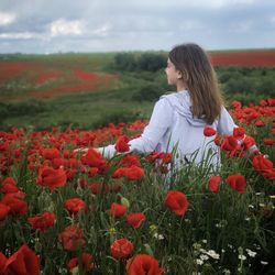 Rear view of woman on red poppy field against sky