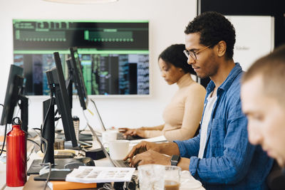 Side view of male with female computer hackers using laptops on desk while sitting in office