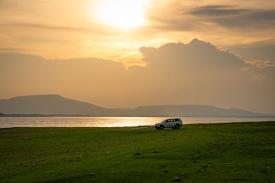 Car running on green meadow near lake at sunset during summer vacation